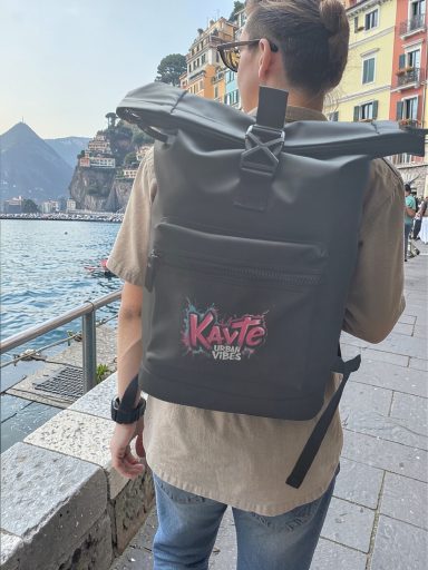 Person mit Rucksack steht am Wasser, farbenfrohe Gebäude im Hintergrund.